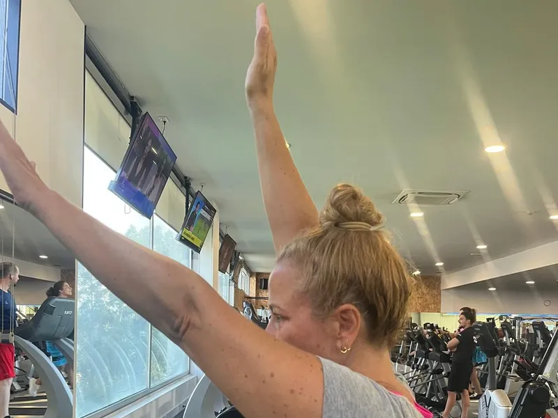 Sócia de braços erguidos acima da cabeça, na sala de exercício
