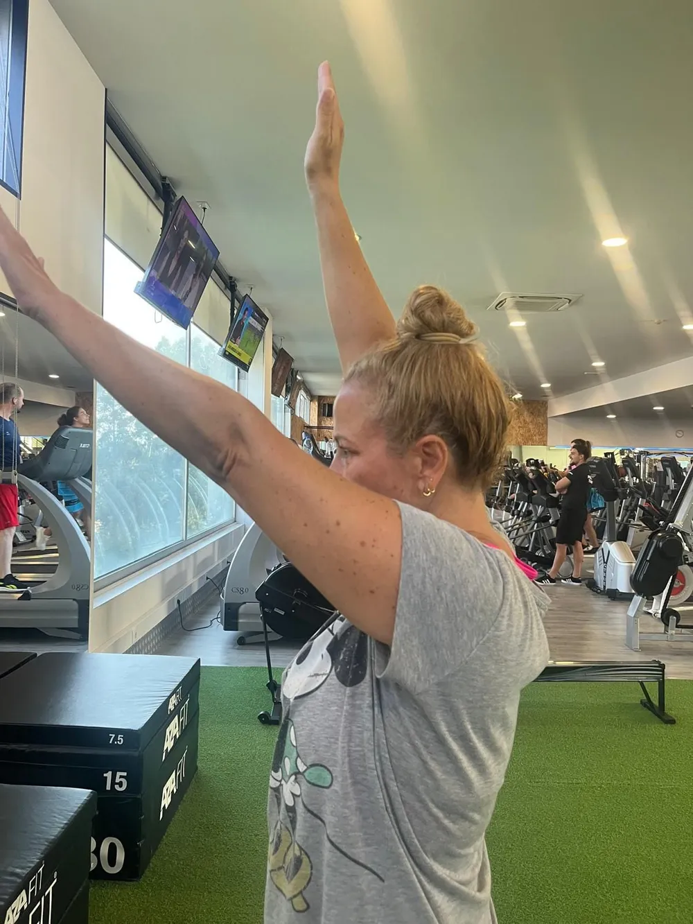 Sócia de braços erguidos acima da cabeça, na sala de exercício