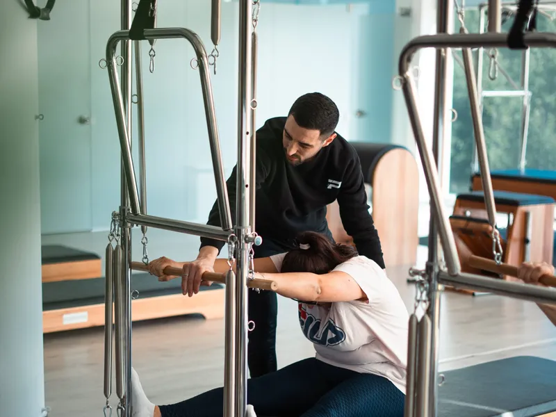 Instrutor a corrigir uma aluna num aparelho de Pilates